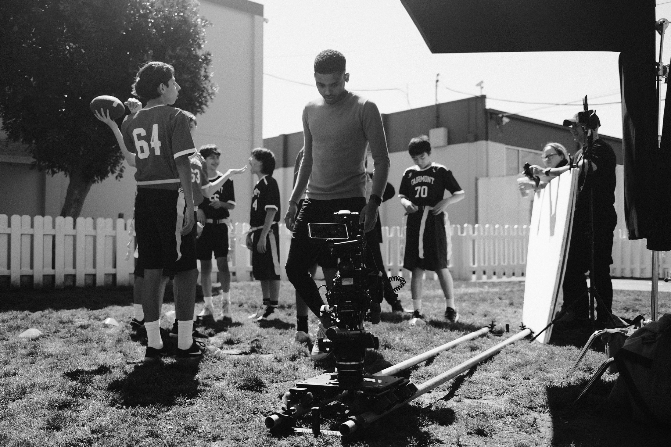 Production crew filming student football players with a camera dolly and lighting equipment